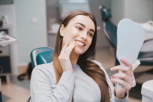 Young woman examining her new smile in a mirror while at the dentist in Fort Collins