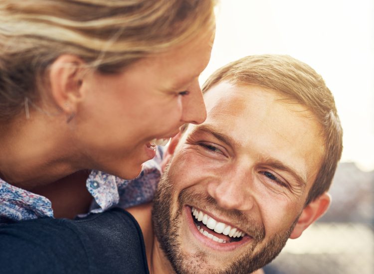 A young man and woman smiling brightly with porcelain veneers.