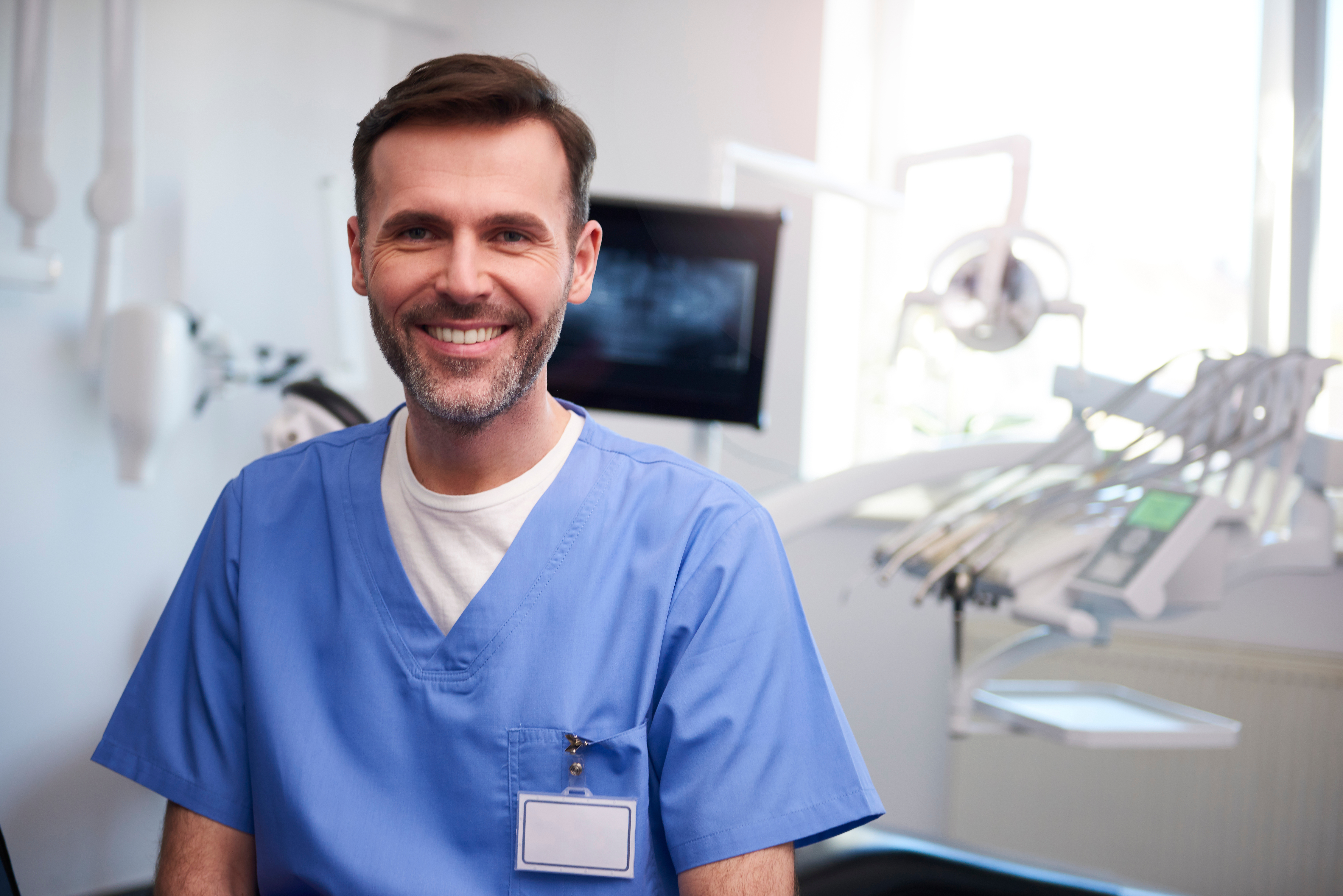 A dentist standing in his office smiling with dental chair in the background