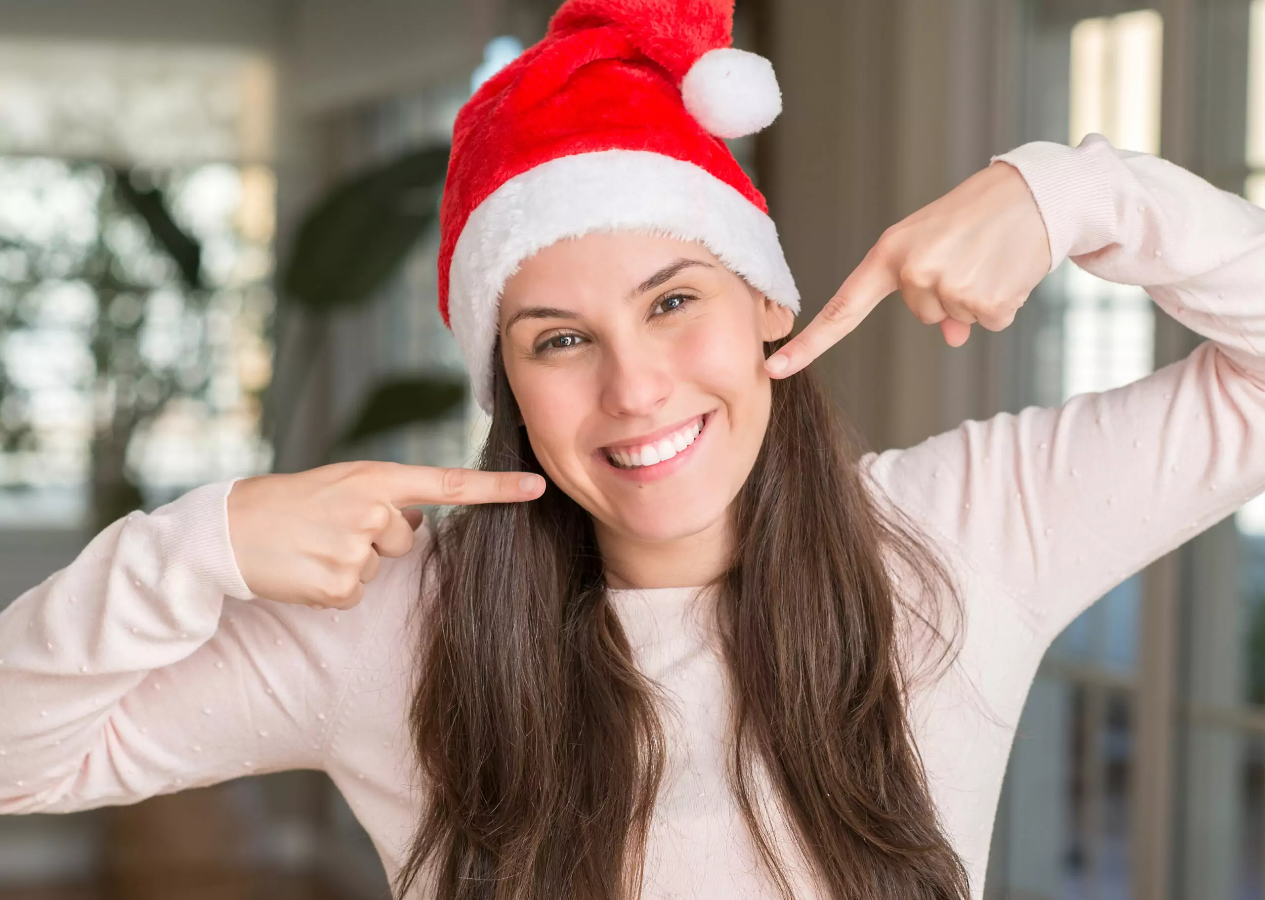 Woman in a santa hat pointing at her straight white smile